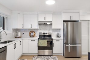 A modern kitchen with white cabinets, stainless steel appliances, and a patterned rug.