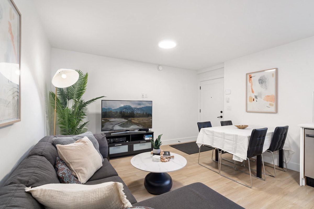 A modern living room with a sofa, coffee table, TV, and dining area.