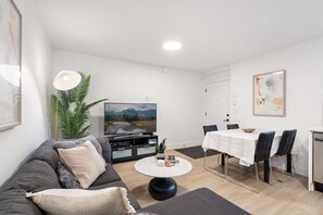 A modern living room with a sofa, coffee table, TV, and dining area.