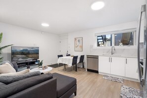 A modern living room with a sofa, a TV, and a dining area with a table and chairs.