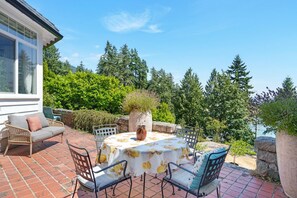 Eine Terrasse im Freien mit Tisch und Stühlen, umgeben von Grünpflanzen und Blick auf Bäume.