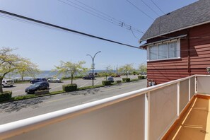 A residential street with parked cars, a clear sky, and a view of the sea. - Waterfront Home on Marine Dr | Steps to the Beach (White Rock)