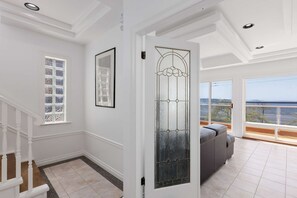A spacious room with a large window offering a view of the sea, a staircase, and a door with a decorative glass panel. - Waterfront Home on Marine Dr | Steps to the Beach (White Rock)