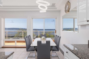 A dining area with a table and chairs, large windows with a view, and a modern chandelier. - Waterfront Home on Marine Dr | Steps to the Beach (White Rock)