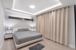 A modern bedroom with a bed, bedside tables, a wall-mounted shelf, and a large window with curtains. - Central Luxury Home - Views and Private Cinema (Vancouver)