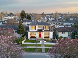 Une maison d’habitation à deux étages, avec une porte rouge, entourée d’une pelouse bien entretenue et d’arbres en fleurs.