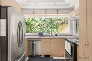 A modern kitchen with stainless steel appliances, wooden cabinets, and a large window with a view of greenery. - Grand 4BR Point Grey Manor - Walk to Beaches (Vancouver)
