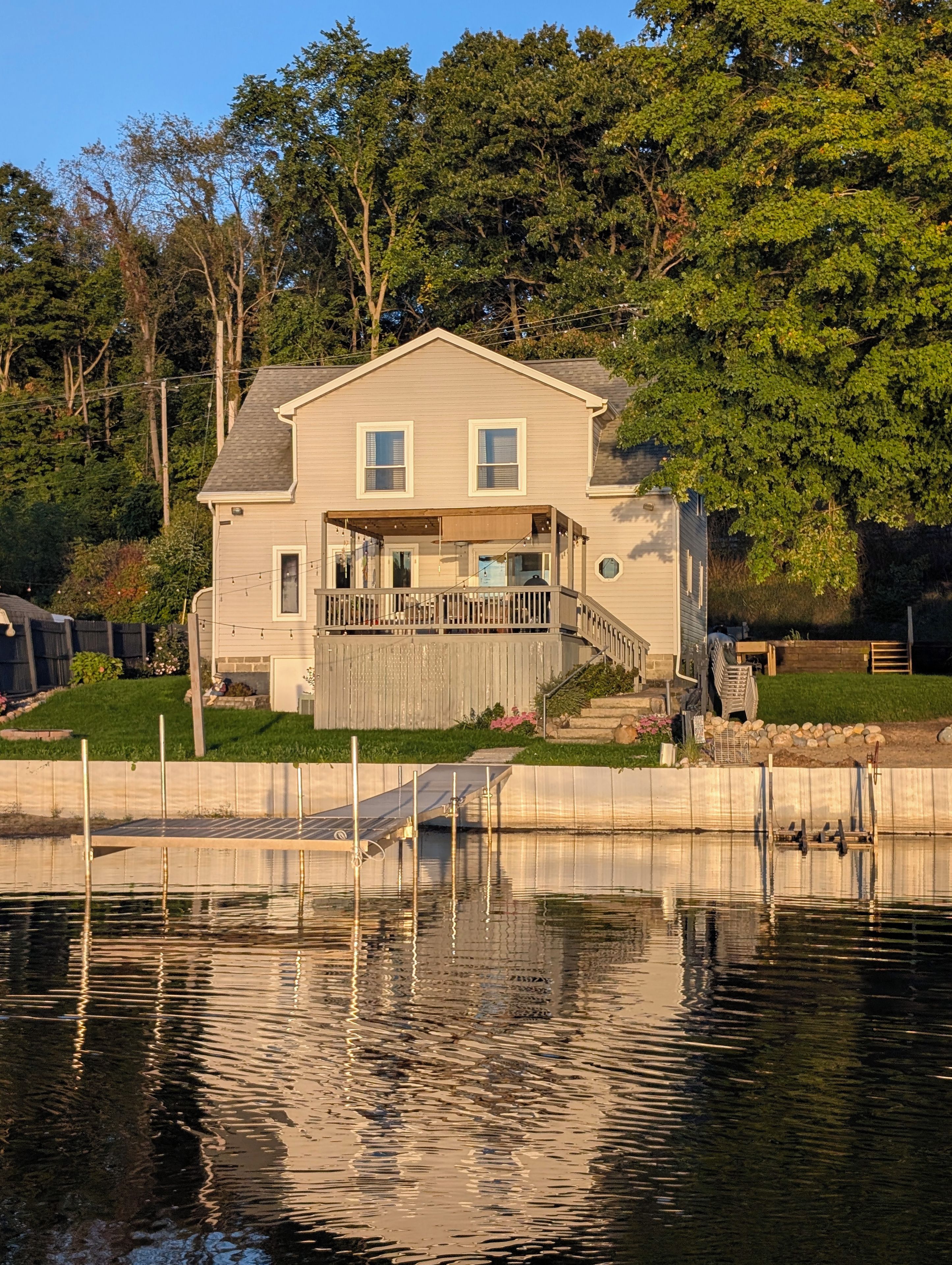 Ein zweistöckiges Haus mit Terrasse, Bootssteg und Teich davor.