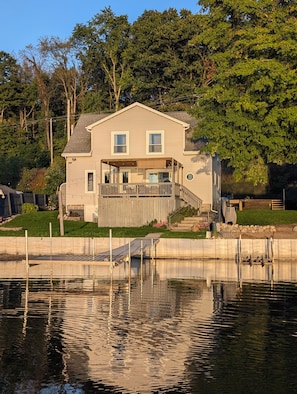 A two-story house with a deck, a dock, and a pond in front. - Dogs Stay Free! Fenced Lakefront House with Deck (Delton)