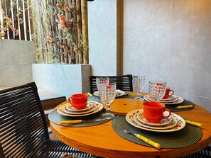 A round wooden table set with red cups, clear glassware, and plates, surrounded by chairs with a woven placemat. - Mirante de Porto Piscinas Naturais (Ipojuca)