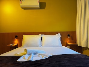 Ein Hotelzimmer mit Bett, Nachttisch, Lampe, Klimaanlage und Vorhang.