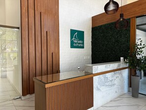 A reception desk with a wooden panel design, a green sign above it, and a green wall with a leafy texture. - Mirante de Porto Piscinas Naturais (Ipojuca)