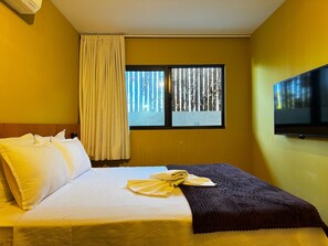 A hotel room with a bed, a window with a view of trees, a flat-screen TV mounted on the wall, and a curtain. - Mirante de Porto Piscinas Naturais (Ipojuca)