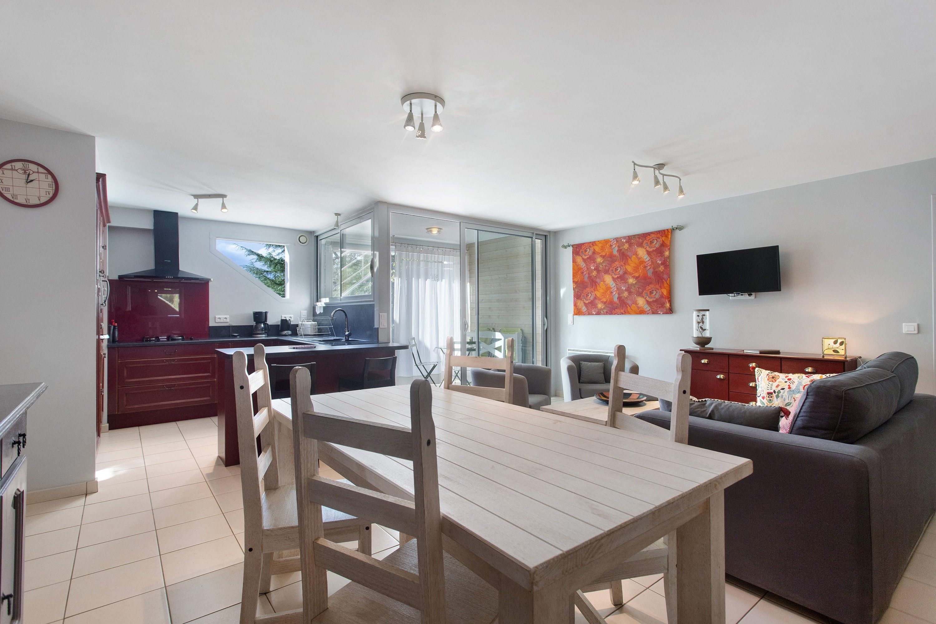 A modern kitchen with a dining area, a sofa, and a TV.