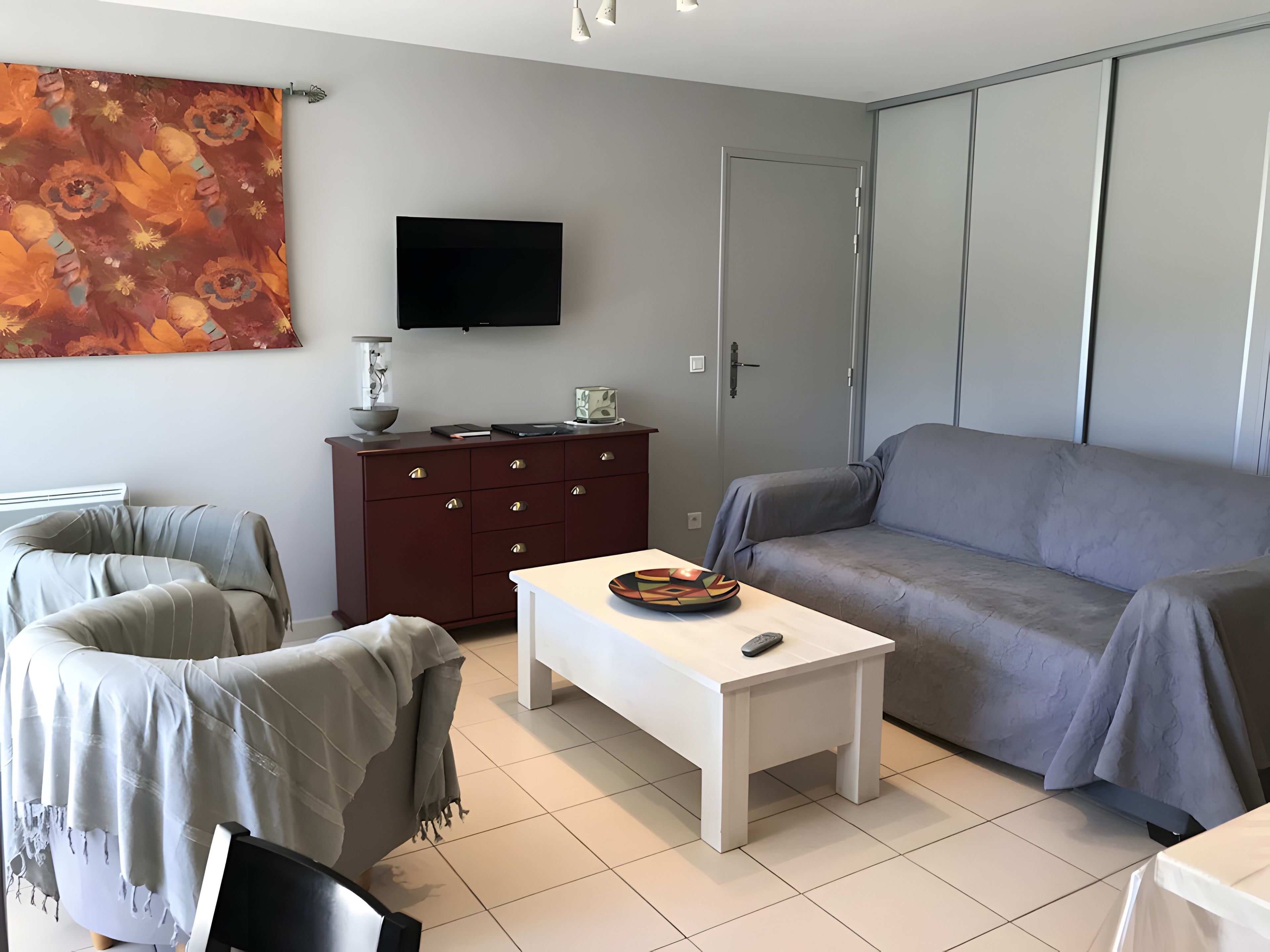 Een moderne zithoek met een bank, een witte salontafel, een donker houten kast en een flatscreen televisie aan de muur.