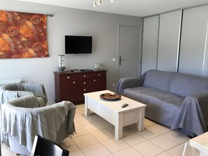 A modern living room with a sofa, a white coffee table, a dark wooden cabinet, and a flat-screen TV mounted on the wall.