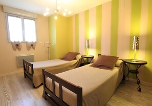 Habitació amb dos llits individuals, un radiador, una finestra amb cortines i una làmpada sobre una taula auxiliar.