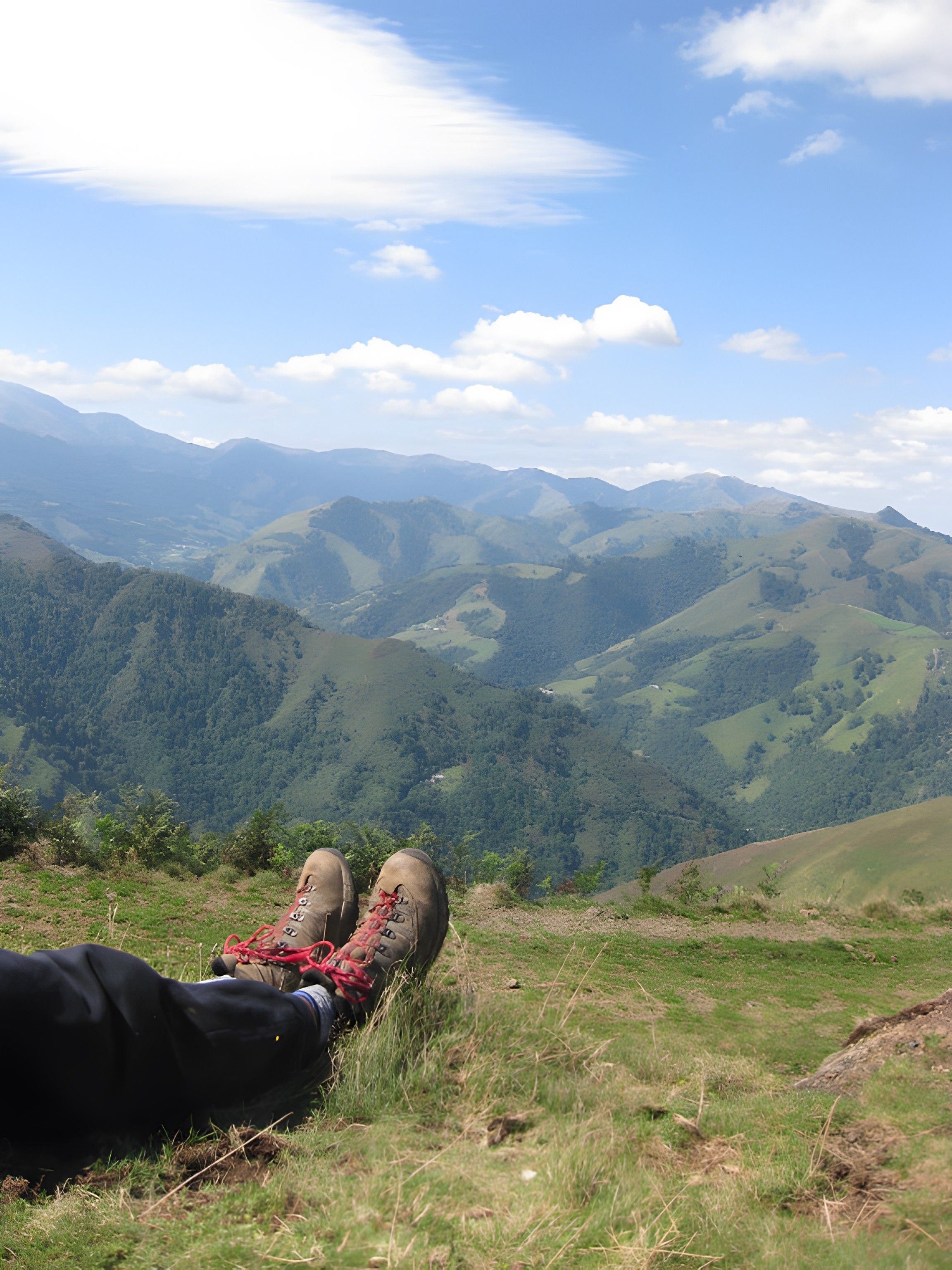 A person lying on a grassy hillside with a view of rolling hills and mountains in the distance.