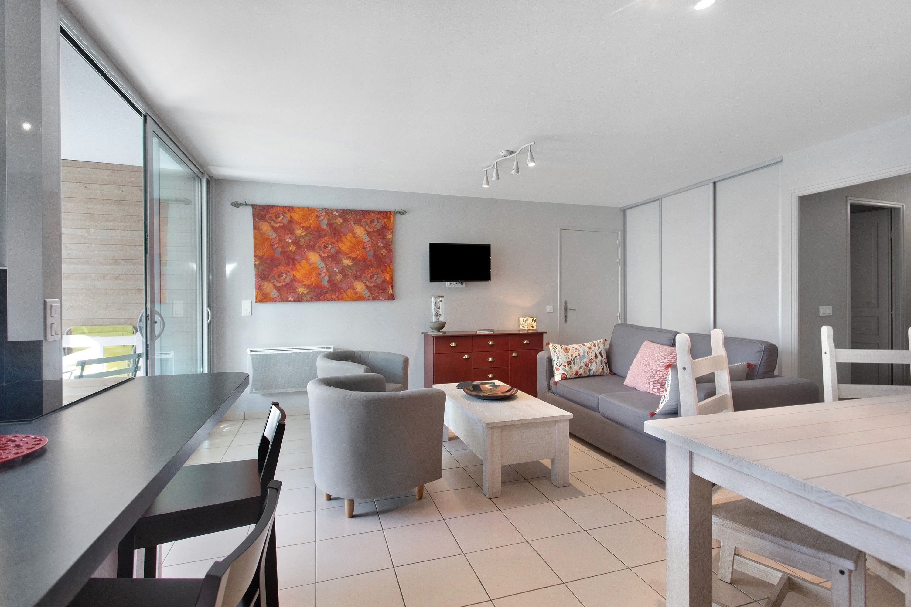 A modern living room with a dining area, a flat-screen TV, and a large window.