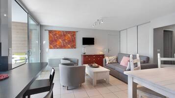 A modern living room with a dining area, a flat-screen TV, and a large window.