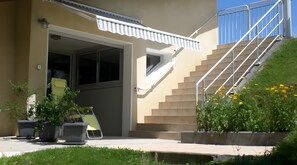 Un edificio con una escalera que lleva a un nivel superior, una puerta con un ventanal y plantas en macetas en el suelo.