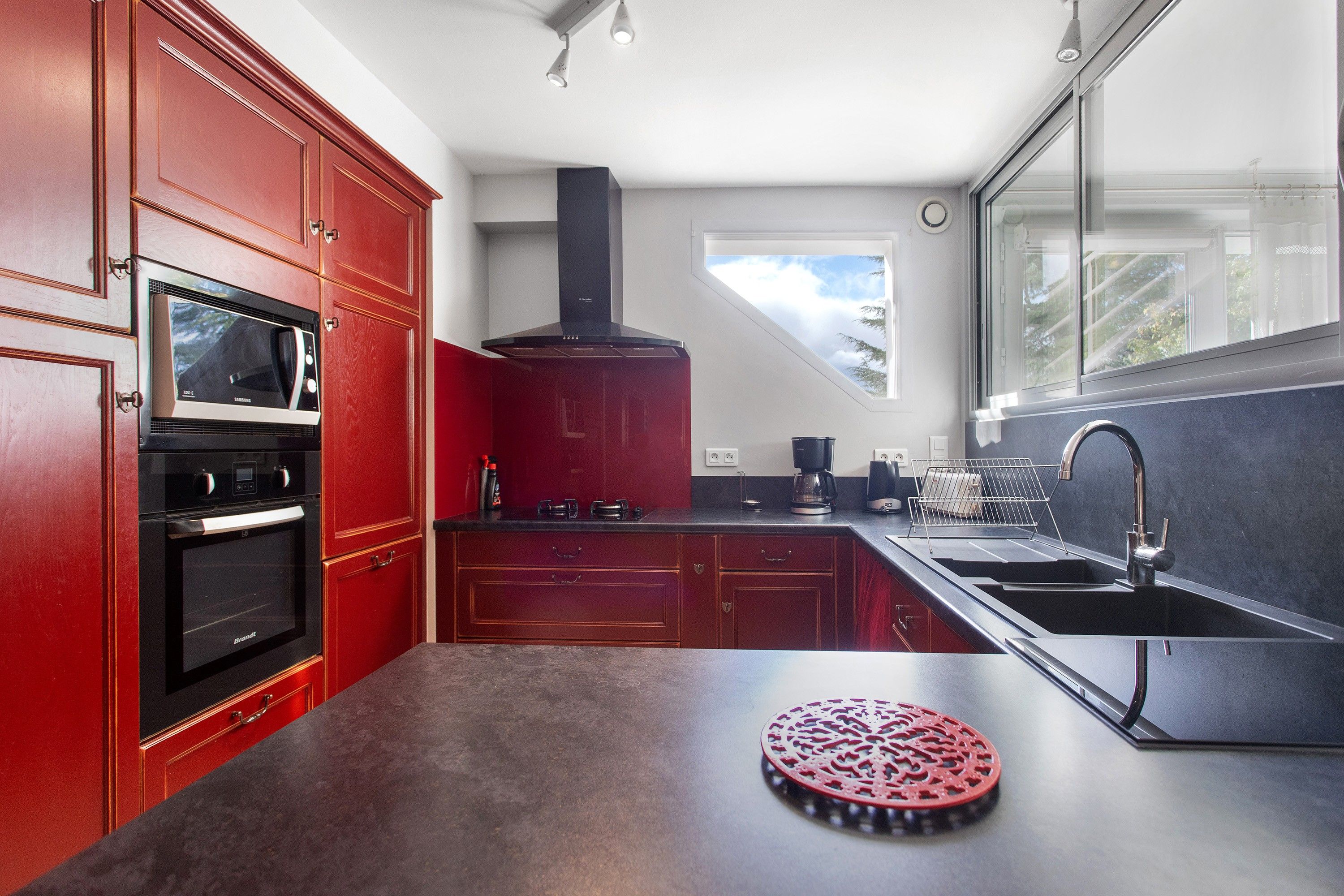 A modern kitchen with red cabinetry, a built-in oven, a microwave, a coffee maker, and a large window.