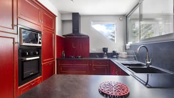 A modern kitchen with red cabinetry, a built-in oven, a microwave, a coffee maker, and a large window.