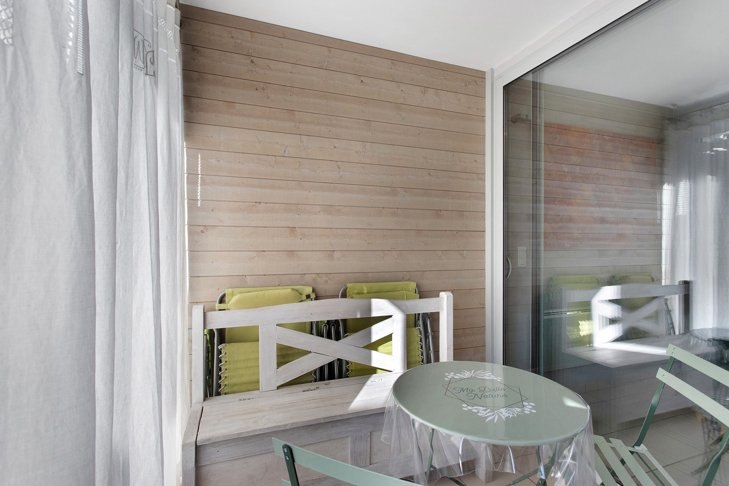 A room with a wooden wall, a window with a view, a small round table, and a white chair.