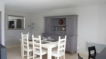 Een eetgedeelte met een witte tafel en stoelen, een grijze kast met planken en een spiegel aan de muur.