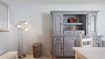 Une pièce avec un meuble gris, un panier en osier, une lampe sur pied et une table en bois.