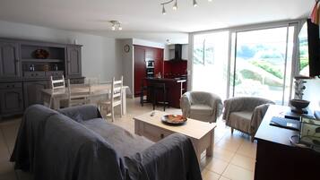 Een moderne woonkamer met een eethoek, keuken en grote schuiframen naar een balkon.