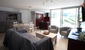 Una sala de estar moderna con comedor, cocina y grandes puertas correderas de vidrio hacia un balcón.