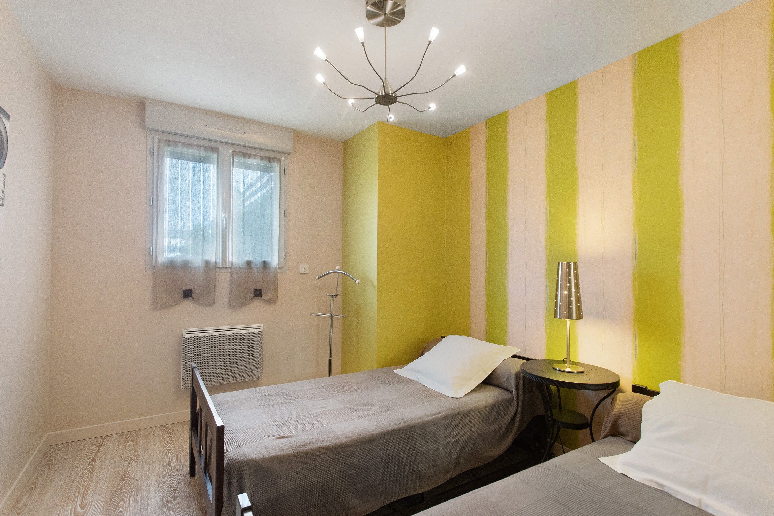 A bedroom with two beds, a radiator, a window with curtains, and a ceiling light fixture.