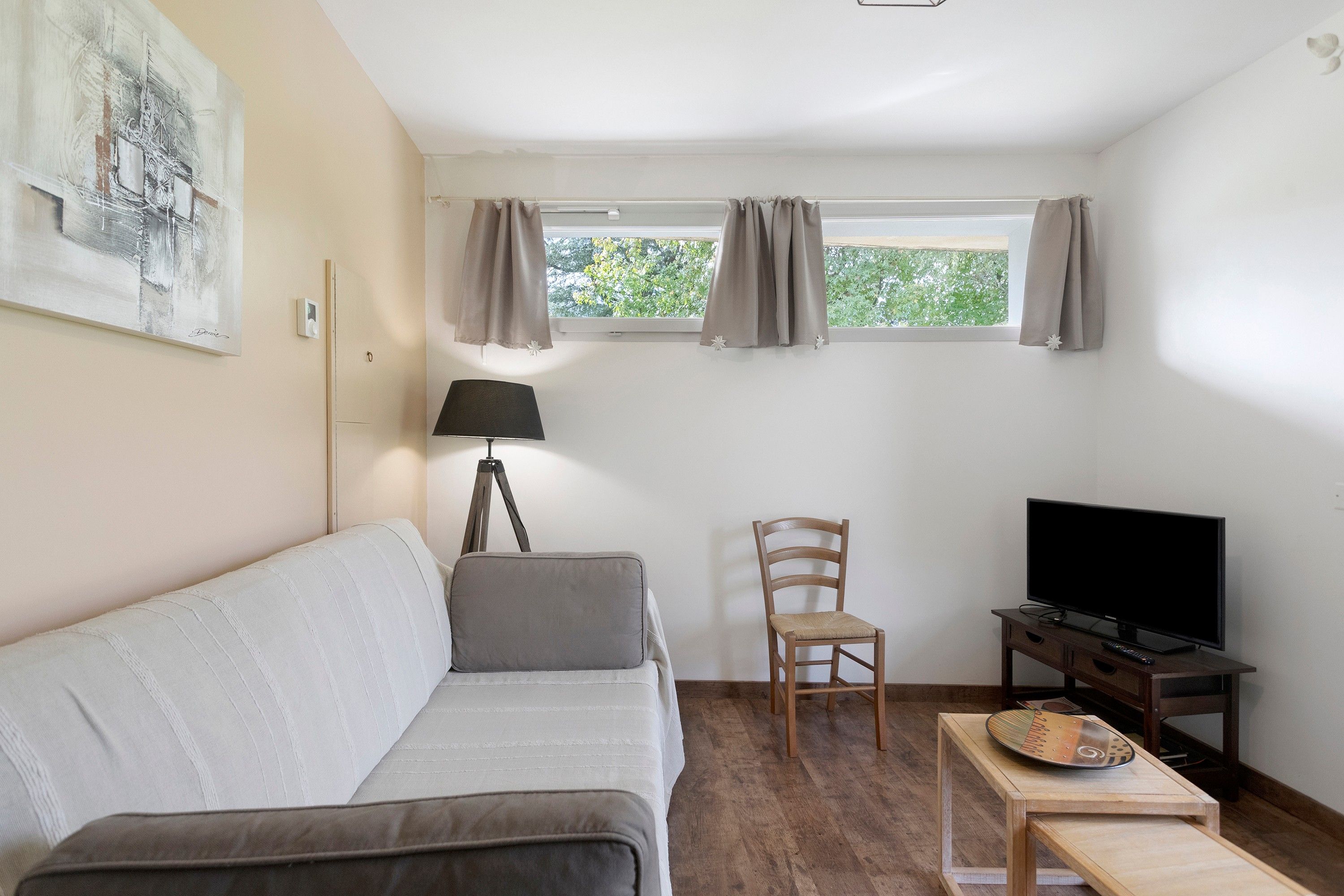 A living room with a sofa, a chair, a TV, a lamp, and a window with curtains.