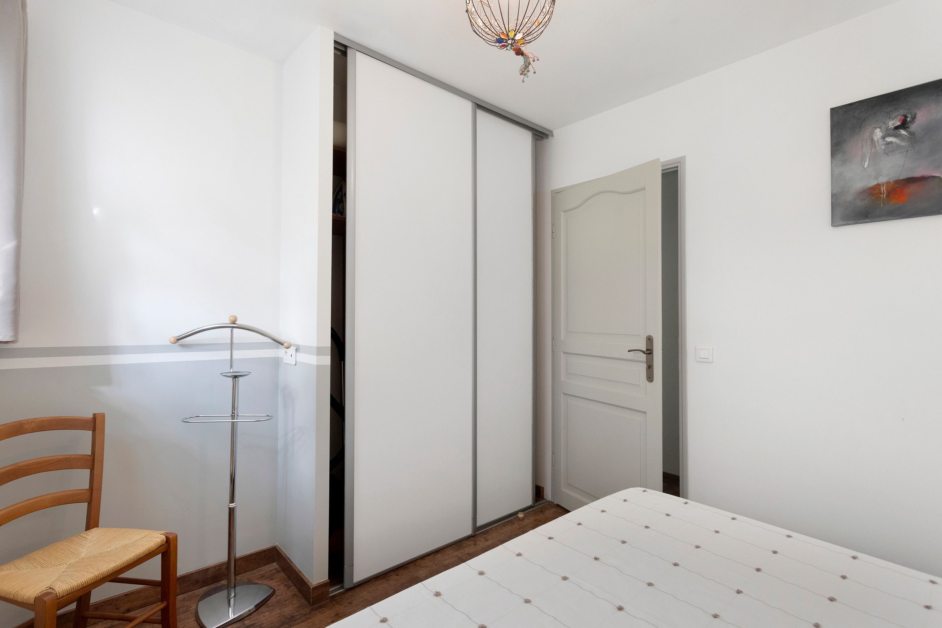 A bedroom with a bed, a chair, a wardrobe, and a door.
