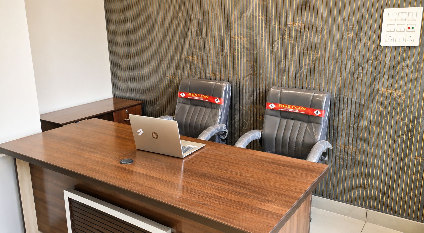 Una sala conferenze con un tavolo in legno, due poltrone in pelle e un portatile HP.