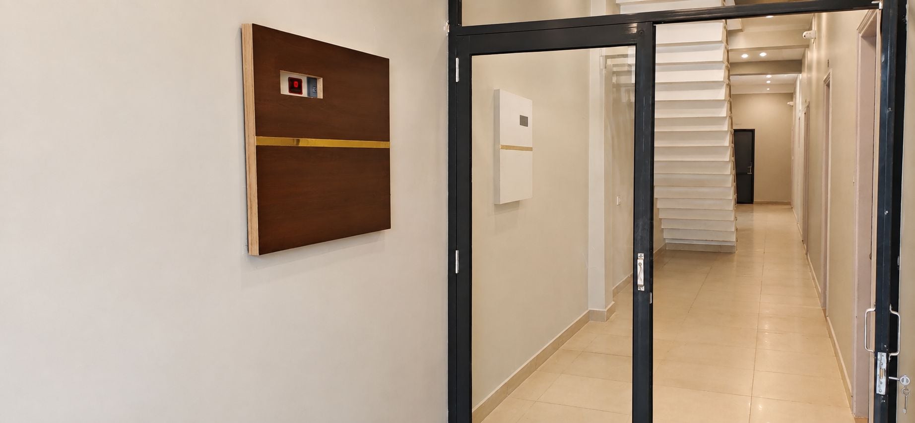En hall med en dörr som leder in till ett rum, en väggmonterad kontrollpanel och en trappa i bakgrunden.
