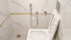 Un baño con inodoro blanco, ducha con cabezal de ducha manual y grifo empotrado en la pared.