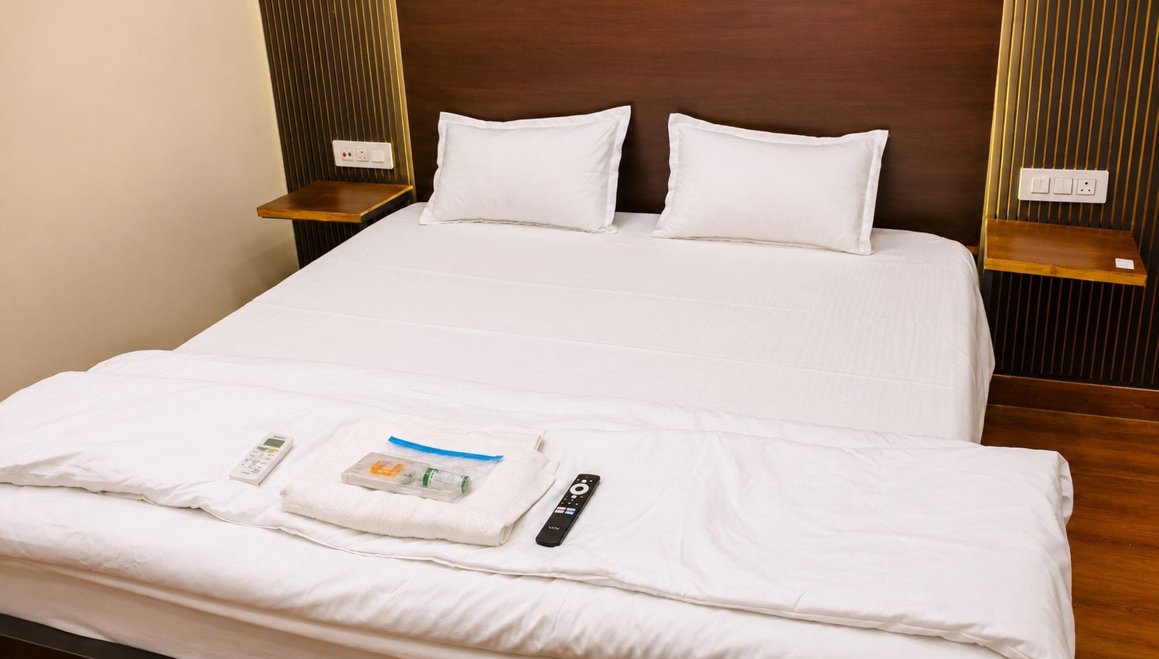 Una cama bien hecha con sábanas blancas, un control remoto y una pequeña botella de loción sobre la cama.