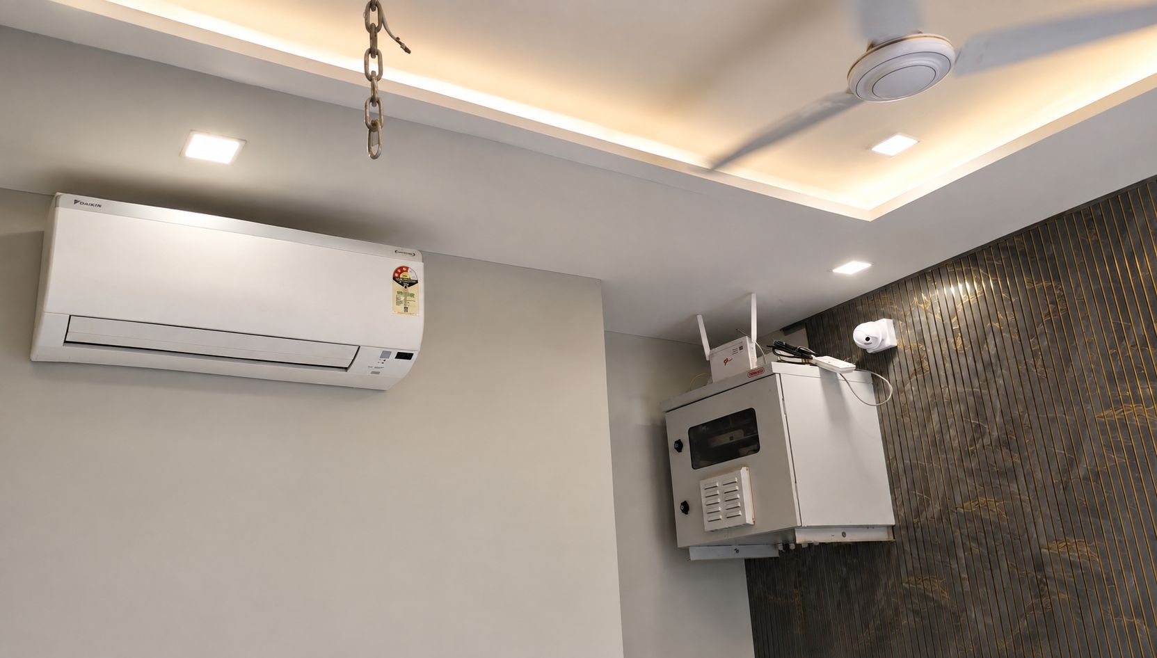 A ceiling-mounted air conditioning unit and a microwave oven in a room with a patterned wall and recessed lighting.