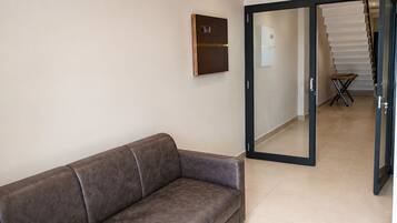 A modern interior with a sofa, a wall-mounted control panel, and a glass door leading to a staircase.