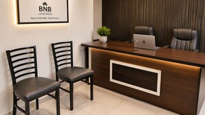 Una recepción con una computadora portátil, dos sillas, una planta en maceta y un letrero que dice 'BNB LUXURY ROOMS Stay Comfortable. Stay Premium'.