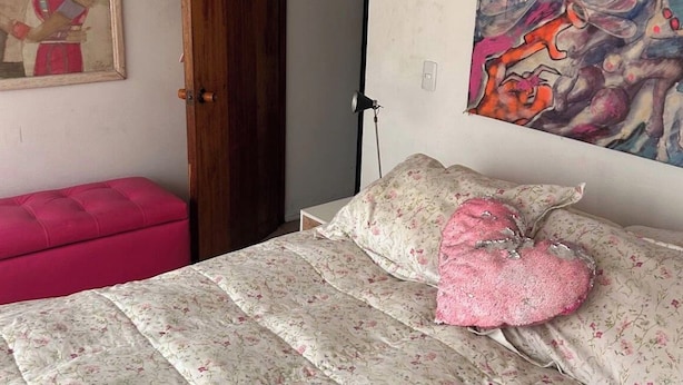 Une chambre à coucher avec un lit, un pouf rose, une porte et un tableau accroché au mur.