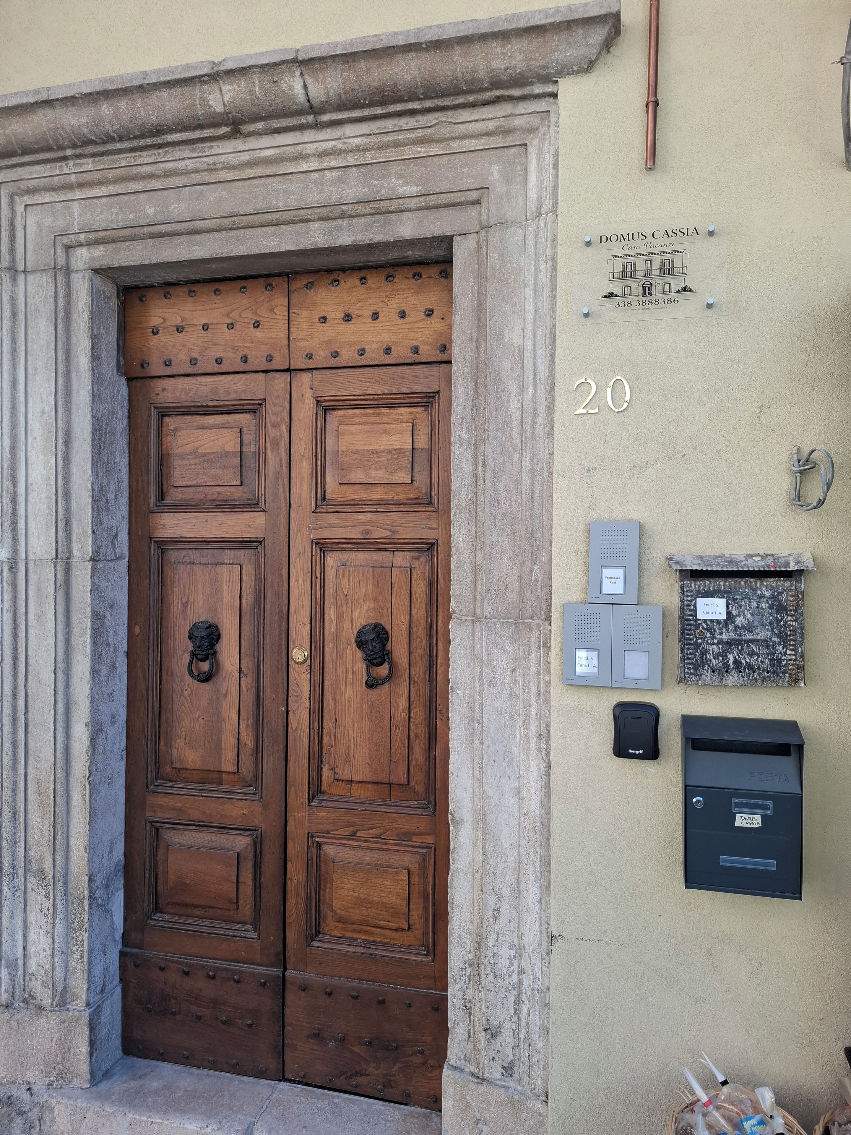 Una porta in legno a due ante con un mormottante a forma di leone, una cassetta delle lettere e un campanello su un muro color beige.