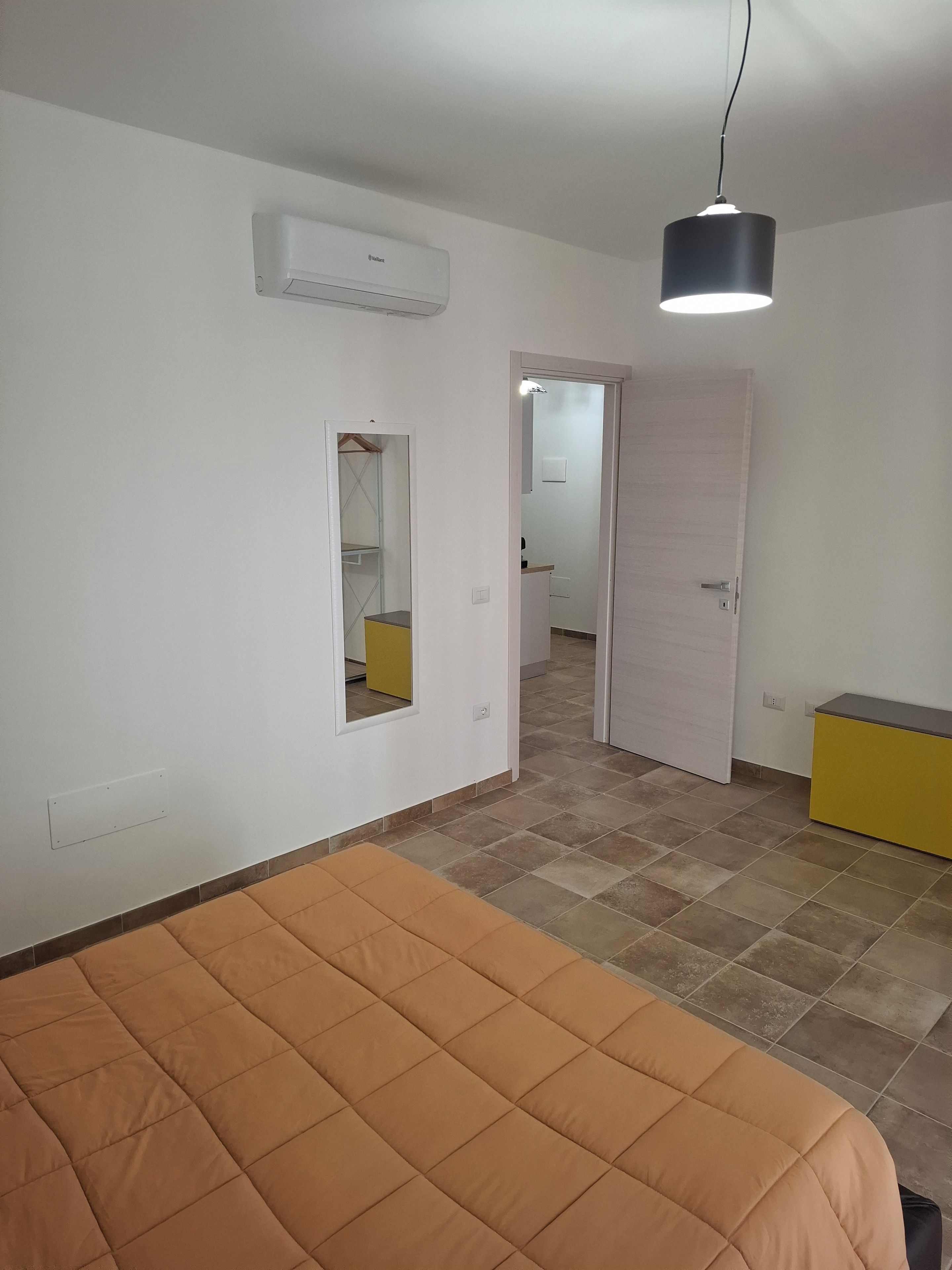 Une chambre à coucher comprenant un lit, une armoire, un miroir et une porte donnant sur une autre pièce.