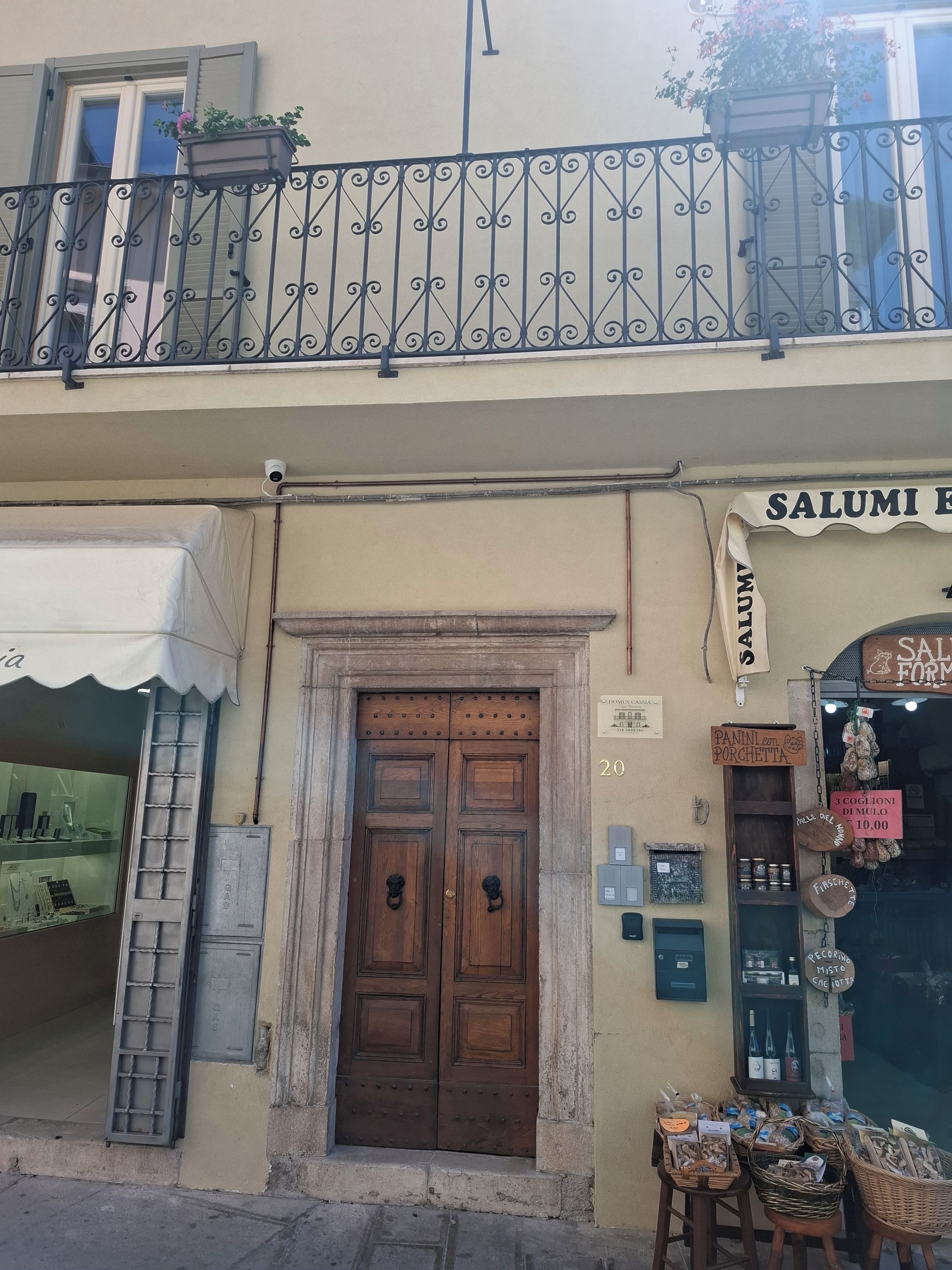 Une devanture de magasin avec une porte à double battant en bois, un balcon orné de balustrades en fer forgé et divers panneaux indiquant les produits et les prix.