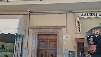 Une devanture de magasin avec une porte à double battant en bois, un balcon orné de balustrades en fer forgé et divers panneaux indiquant les produits et les prix.