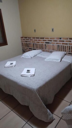 Una cama individual con cabecera de ladrillos y colcha gris.
