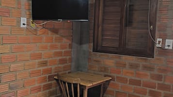 Et værelse med en murstensvæg, et fladskærms-tv monteret over et træbord og en stol, en klimaanlæg og en seng med mønstret sengetøj.