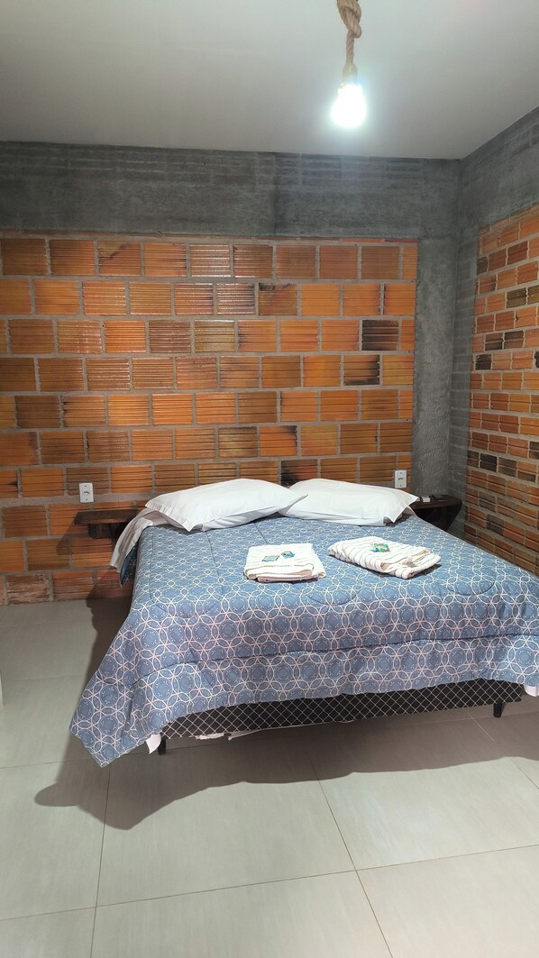 Una habitación con pared de ladrillo visto, cama con colcha estampada y lámpara colgante.
